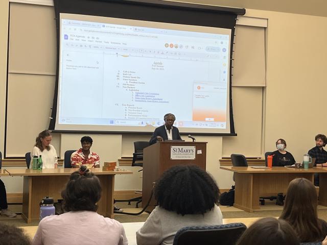 President Jordan speaks at a podium in front of SGA members 