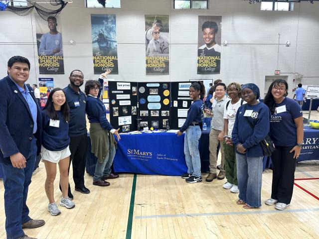 Four people standing on the left of a table and five people standing on the right side of a table in a gymnasium