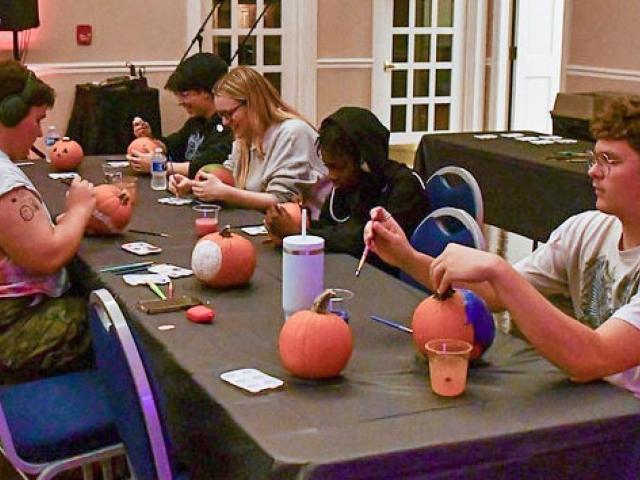 Several students seated at table decorating pumpkins