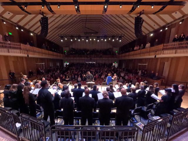 View from back of stage showing chorus and orchestra perform before packed concert hall