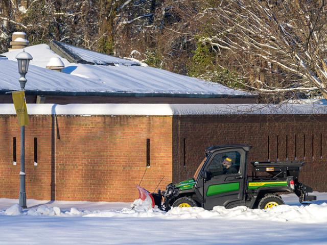 Two men in a "gator" clear snow in front of Montgomery Hall