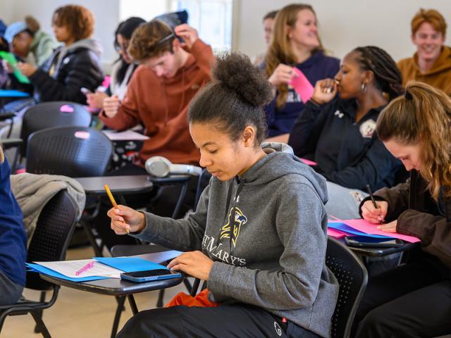 Students seated at desks writing cards