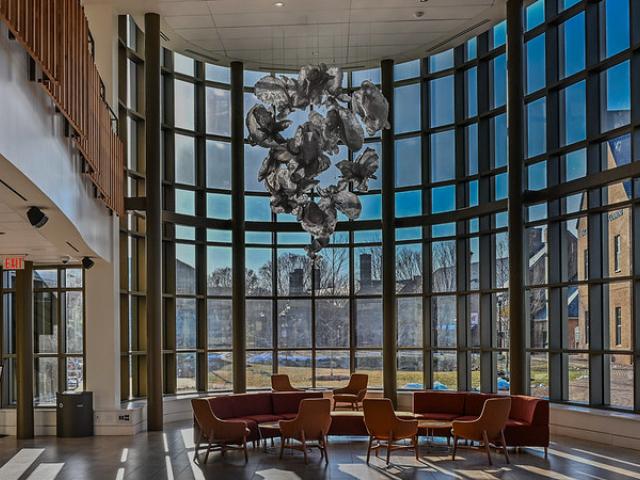 A spacious lobby featuring large windows and comfortable chairs, inviting natural light and providing a welcoming atmosphere. Oysters sculpture suspended from the ciling.