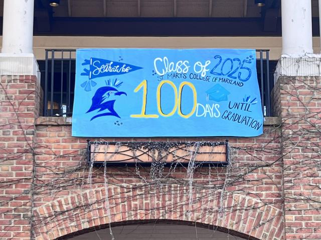 A brick building with a blue and yellow banner hanging on the balcony. The banner reads, "Class of 2025" with "100 Days Until Graduation" underneath, and "Seahawks" with a bird logo on the left.