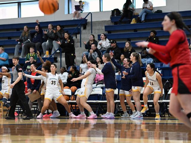 Basketball team members cheer from the bench in front of crowd