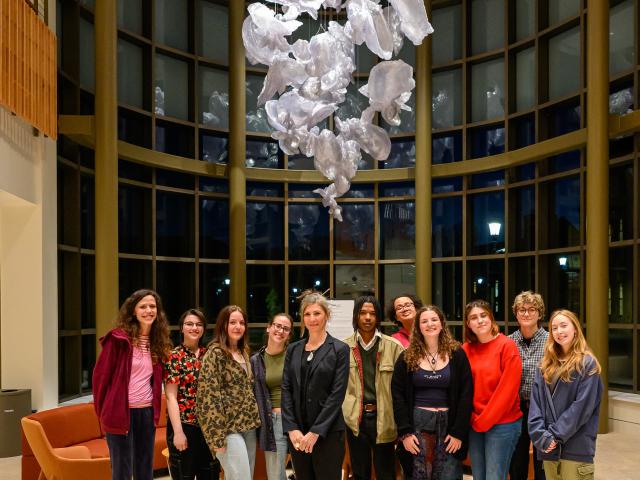 A group of eleven people standing together indoors under a ceiling art installation of translucent shapes.