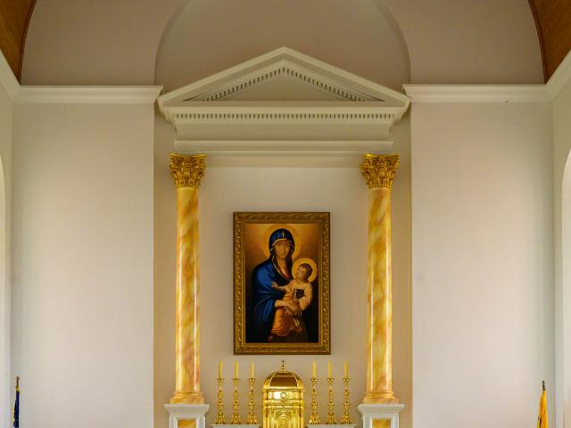 A framed painting of Madonna and Child hangs between two gold columns above a gold tabernacle and candlesticks in a church interior.