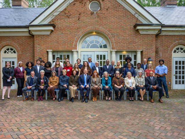 A group of people pose for a formal photo in front of a brick building with arched windows and doors.