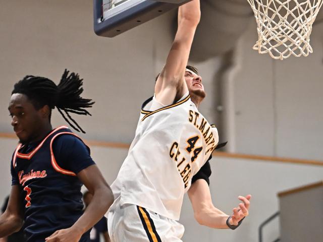A basketball player in a white uniform attempts a layup while a defender in a dark uniform tries to block during a game.