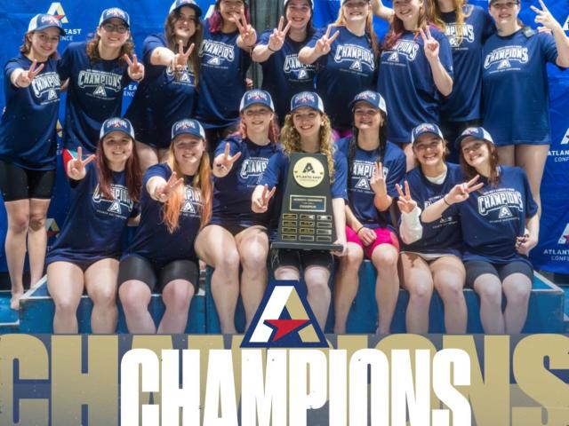St. Mary’s women’s swim team poses with a championship trophy and medals in front of a branded backdrop, celebrating their 2026 Atlantic East Conference win.
