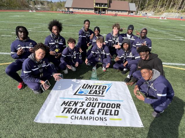 A men's track and field team poses on a field behind a banner that reads "United East 2026 Men's Outdoor Track & Field Champions."