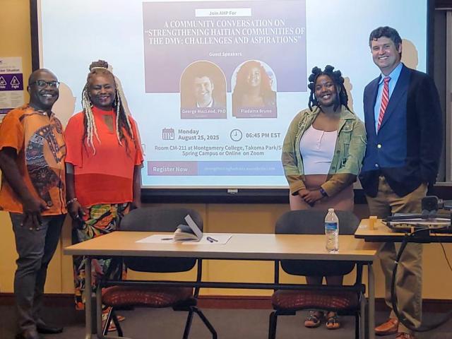 Four people stand in front of a projector screen displaying information about a community conversation event at Montgomery College. A table with chairs is in the foreground.