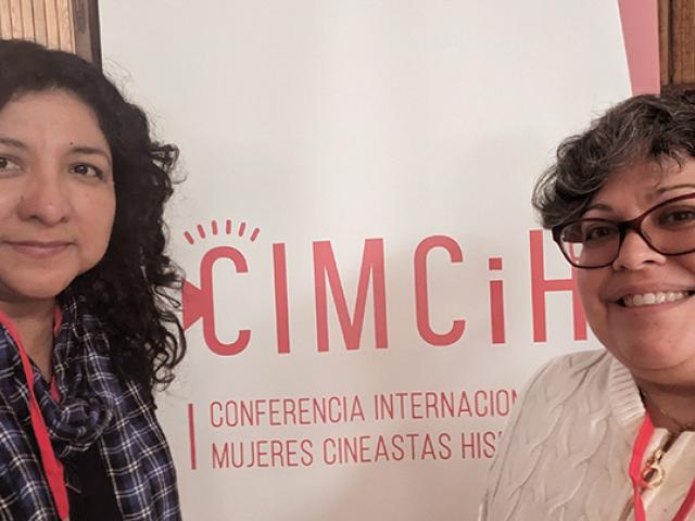 Two women stand in front of a CIMCiH banner at a conference for women filmmakers and historians.
