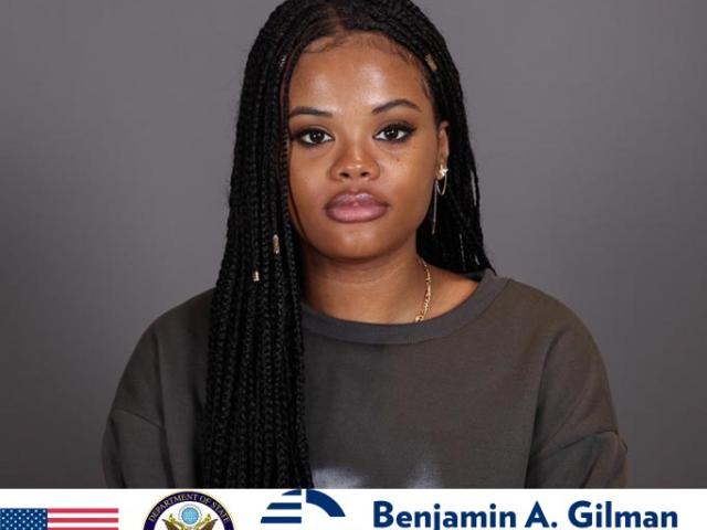 A woman with long braided hair looks at the camera against a plain background. The Benjamin A. Gilman International Scholarship logo and US symbols appear at the bottom.