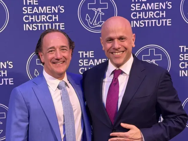 Two men in suits pose and smile in front of a step-and-repeat backdrop with "The Seamen's Church Institute" logo and text.