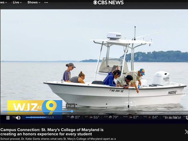 Four people examine something on a small white boat on the water during a CBS News segment about St. Mary’s College of Maryland.