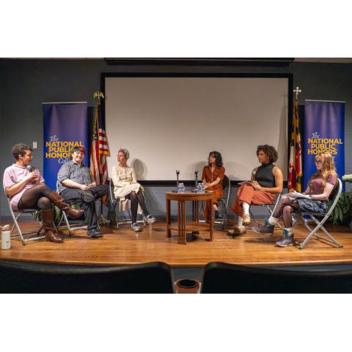 Six people sit on a stage in a discussion panel setup, with two "National Public Housing Museum" banners and American flags in the background.