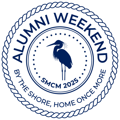 Navy blue circular logo with a heron silhouette in the center surrounded by the text "ALUMNI WEEKEND SMCM 2025" at the top and "BY THE SHORE, HOME ONCE MORE" at the bottom, framed by a rope-like border.