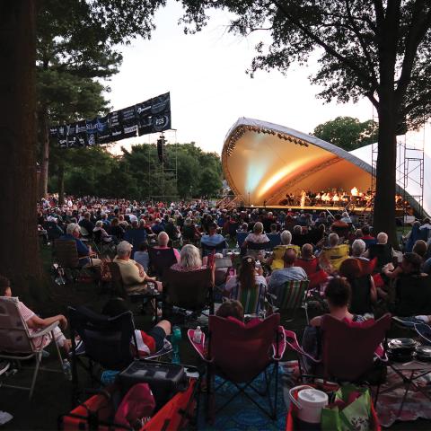 A large audience sits on lawn chairs and blankets at River Concert Series