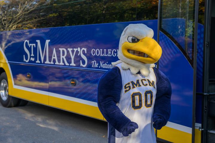 Solomon the Seahawk stands in front of a St. Mary's College River Runner bus.
