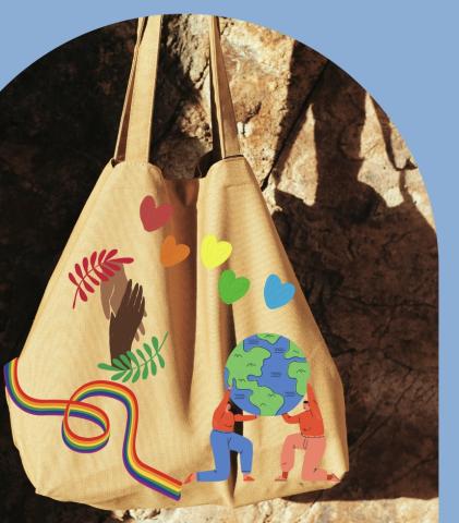 A tan tote bag with handles is decorated with colorful hearts, a rainbow ribbon, hands, and cartoon figures holding a globe, set against a stone background.