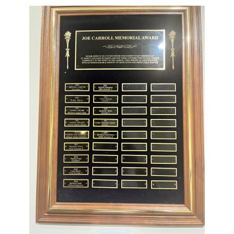 A wooden plaque titled "Joe Carroll Memorial Award" displays engraved nameplates in several rows, with some blank spaces.