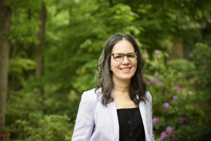 A woman smiling in front of trees.