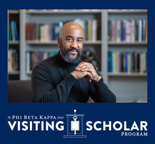 A person with a beard and black turtleneck sits at a table, smiling, in front of a bookshelf. Text reads: “Phi Beta Kappa Society Visiting Scholar Program.”.