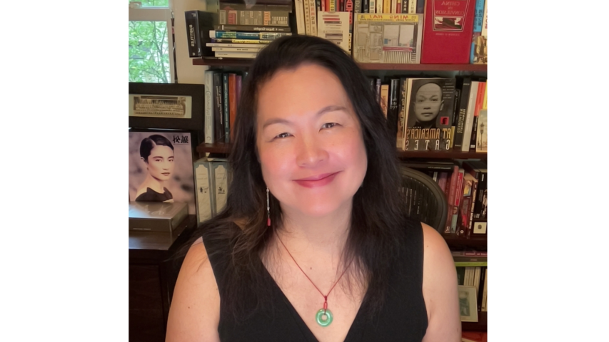 Dr. Chow with long dark hair smiles at the camera, seated in front of bookshelves filled with books and framed photos.