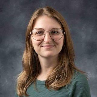 A person with long brown hair wearing round glasses and a green shirt.