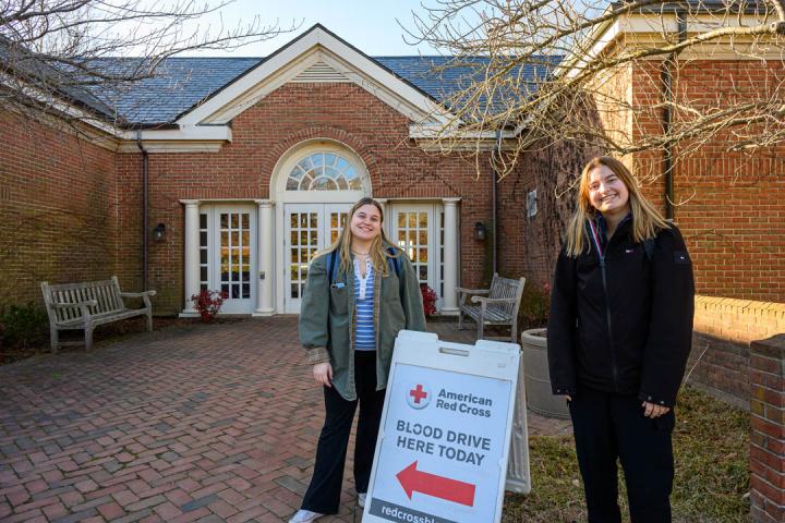 Two students standing in front of building next to sign advertising American Red Cross blood drive