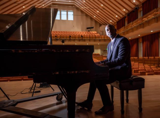 Ellington Carthan seated at piano on stage with empty peformance venue in background