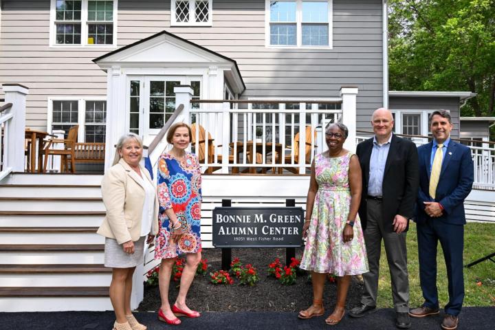 Five people stand in front of the Bonnie M. Green Alumni Center, posing for a photo near the building's entrance and a sign with the center's name.