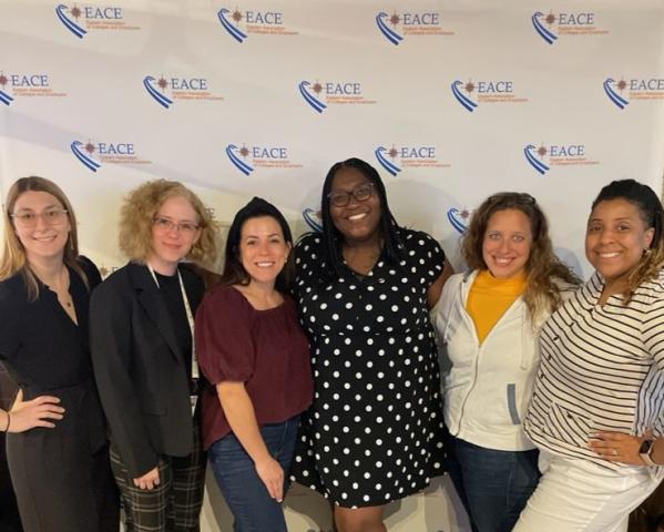 Six women standing together and smiling in front of a backdrop with EACE logos.