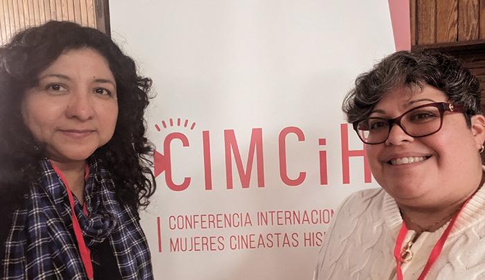 Two women stand in front of a CIMCiH banner at a conference for women filmmakers and historians.