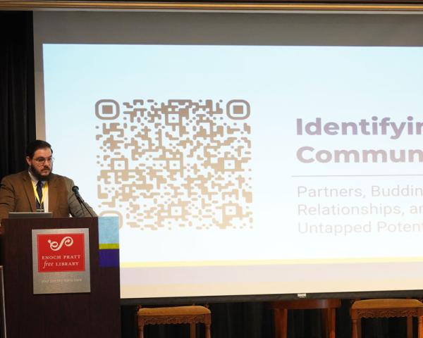 Shane Moran stands at a podium giving a presentation projected on the screen behind them.