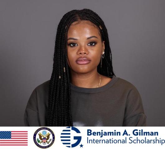 A woman with long braided hair looks at the camera against a plain background. The Benjamin A. Gilman International Scholarship logo and US symbols appear at the bottom.