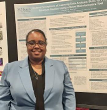 A person wearing glasses and a light blue blazer stands in front of a scientific research poster.