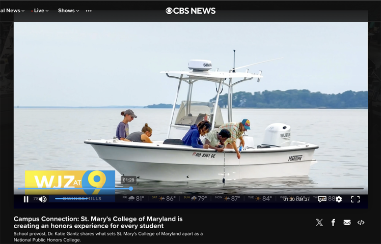 Four people are on a small white boat on a calm body of water under a cloudy sky. The boat has a canopy and is labeled “MD 8091 BE.” The CBS News logo is visible at the top of the image.