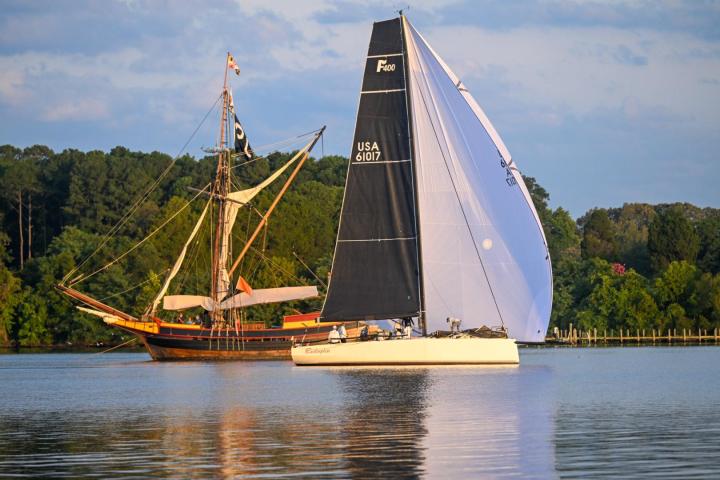 A sail boat with black and white sails passes the Maryland Dove talliship on the St. Mary's River 