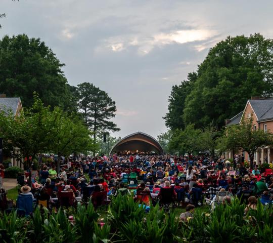 A large crowd sitting in lawn chairs facing an outdoor amphitheater stage.
