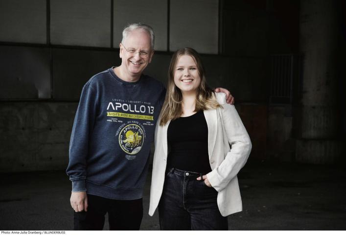 An older man in an Apollo 13 sweatshirt and a young woman in a blazer stand side-by-side, smiling for a photo.