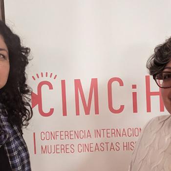 Two women stand in front of a CIMCiH banner at a conference for women filmmakers and historians.