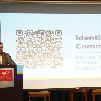 Shane Moran stands at a podium giving a presentation projected on the screen behind them.