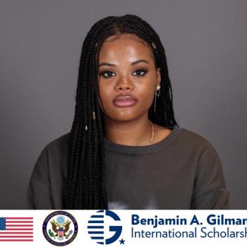 A woman with long braided hair looks at the camera against a plain background. The Benjamin A. Gilman International Scholarship logo and US symbols appear at the bottom.