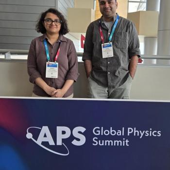 Drs. Shalini Ganguly (left) and Anish Agashe (right) stand behind a banner that reads "APS Global Physics Summit," each wearing conference badges.
