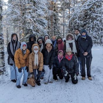 A group of fourteen people dressed in winter clothing pose for a photo on a snowy path surrounded by snow-covered trees.