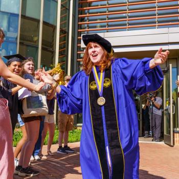 President Rhonda Phillips celebrates outside a building while a group of people clap and cheer.
