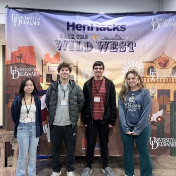 Four students stand in front of a "Hack the Wild West" HenHacks banner at the University of Delaware.