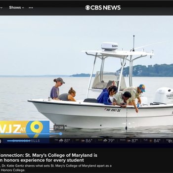 Four people examine something on a small white boat on the water during a CBS News segment about St. Mary’s College of Maryland.